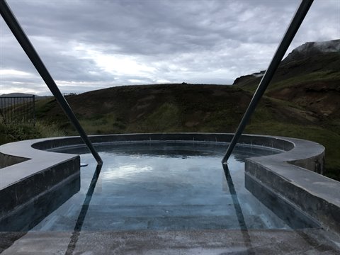 Piscina termale in pietra tra le colline vulcaniche sotto nuvole grigie