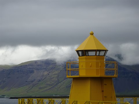 Faro giallo sotto nuvole basse, montagne nebbiose sullo sfondo, Siglufjordur