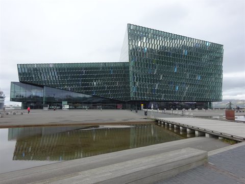 Facciata di vetro Harpa a Reykjavik sotto cielo grigio, riflessa nell'acqua