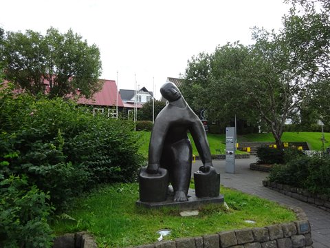 Statua bronzea di donna con bidoni tra i verdi giardini di Reykjavik