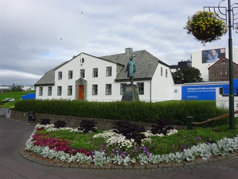 Casa bianca con tetto verde e statua di bronzo, aiuole fiorite a Reykjavik