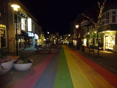 Pedestrian street painted with rainbow asphalt, lit shops and fairy lights at night