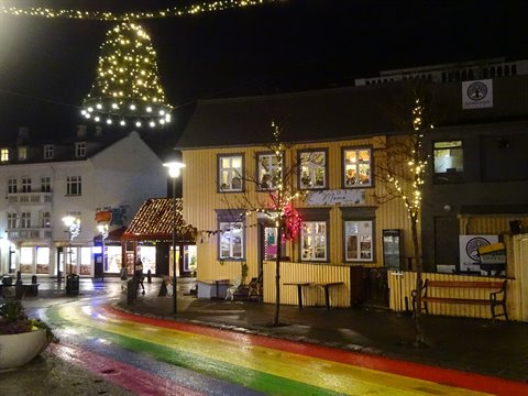 Rainbow-striped street in front of illuminated yellow wooden house at night