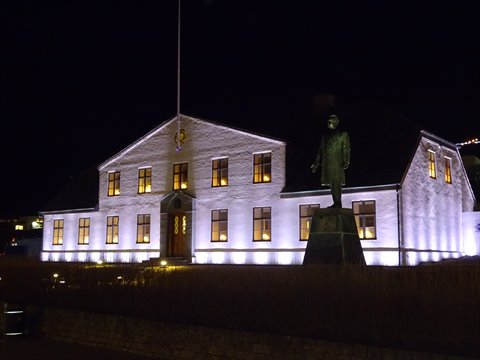Illuminated white building at night with statue in foreground, warm artificial light