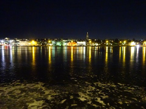 Lit city at night reflected on frozen water, colorful lights along the lakefront