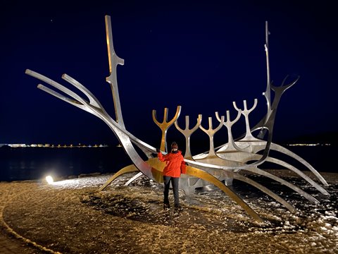 Traveler in red jacket beside a steel boat sculpture at night