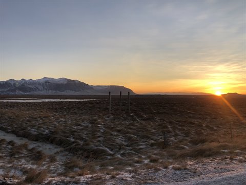 Frozen field with snowy mountains on the horizon, low sun lighting dry grass
