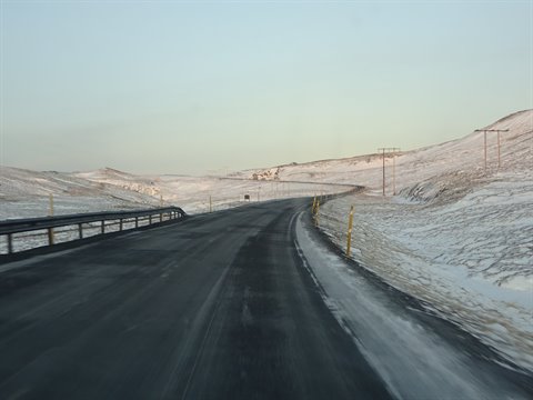 Asphalt road curving through snowy hills, telephone poles, pale morning light