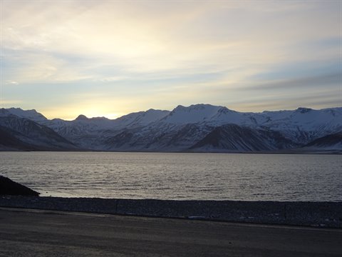 snowy mountains before calm sea under bright cloudy sky