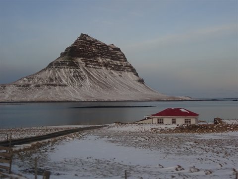 Red-roofed house in snow before steep mountain, cold morning light
