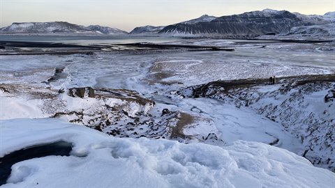 Traveler on snowy edge observes icy valley and mountains under pale sky