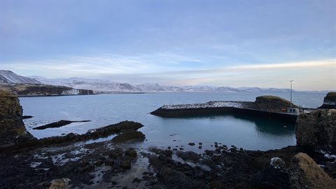 Snowy bay between black rocks, calm water, blue sky, cold light