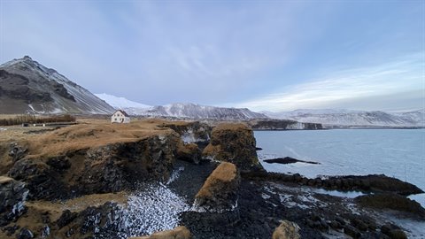 Lone white house on snowy cliffs above frozen bay under cloudy sky