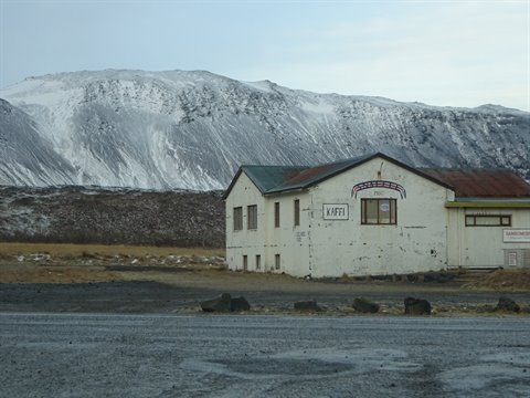 Old white building with Kaffi sign in front of snowy mountain, cold light
