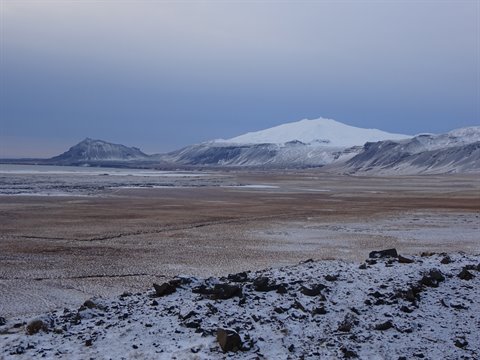 Snowy mountains above brown plain under grey sky, cold diffuse light