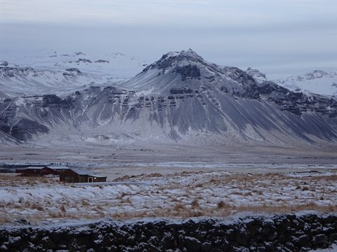 Snowy mountains over a golden field with a stone farm, cold light
