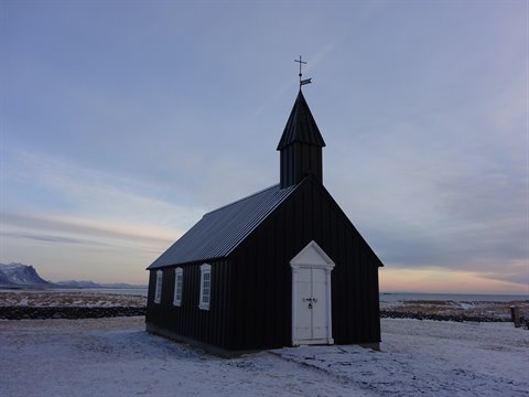 Black wooden church on snow, mountains and pastel sky, cold light