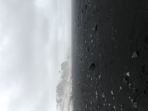 Black sand beach with scattered rocks under a cloudy sky