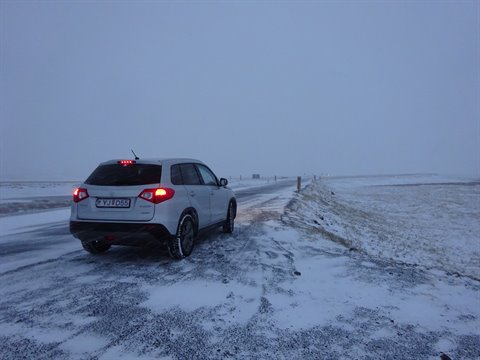 SUV parked on snowy road, rear lights on, foggy winter weather