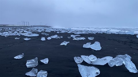Translucent ice chunks on black sand under grey sky and fog