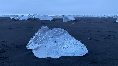 Large translucent ice blocks on black volcanic sand, diffused overcast light
