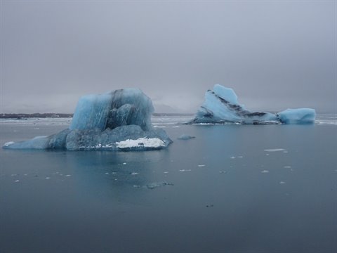 Blue icebergs float on grey waters under cloudy skies