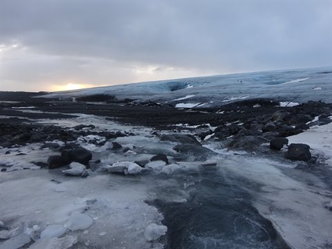 Glacier among volcanic rocks and ice under cloudy sky, low cold light