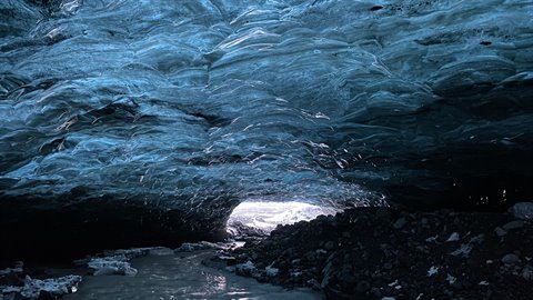 Inside a blue ice cave, light entering through the opening