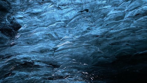 Blue glacier ice with rippled surfaces, cold light filtering through dark crevices