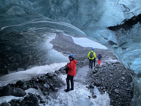 Helmeted hikers explore inside a blue ice cave over snowy rocks