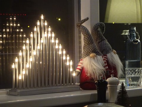 Lit Christmas candle arch and red gnomes on indoor windowsill at night
