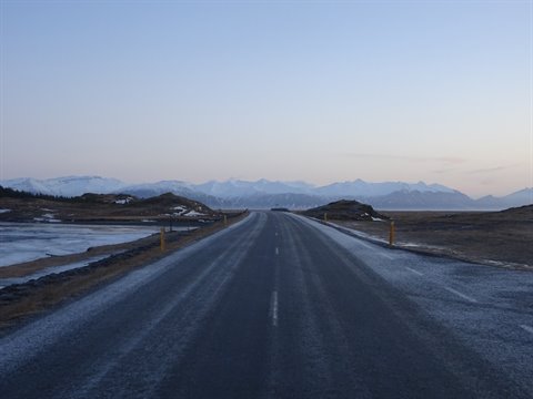 Straight asphalt road toward snowy mountains, cold dusk light