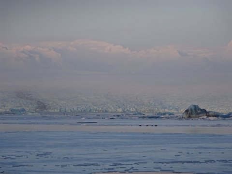 Glacier and sea ice under soft light, snowy mountains veiled in haze