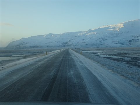 Snowy road driven by car toward snow-covered mountains, cold morning light, travel journal