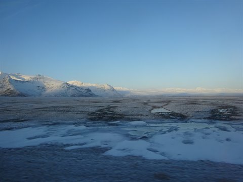 Snowy plain and snow-capped mountains on the horizon under blue sky, cold morning light
