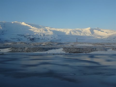 Snowy mountains behind frozen lake, golden light on peaks, blue sky