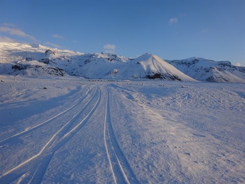 Ski tracks on snow leading toward snowy mountains under blue sky, morning light