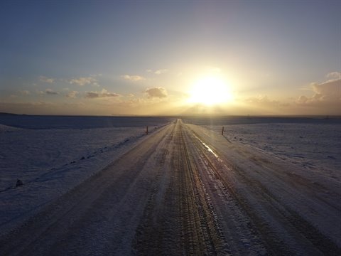 Straight snowy road across icy plain, low sun lighting the tire tracks