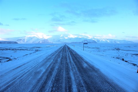Straight snow-covered road toward white mountains under blue sky, cold morning light
