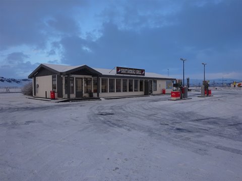 Service station with fuel pumps, scattered snow, cold twilight light