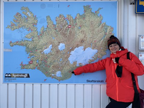 Traveler in red jacket pointing at a physical map of Iceland on a wall, daylight