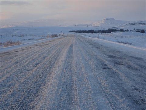 Snow-covered road with distant car among frozen hills, cold morning light
