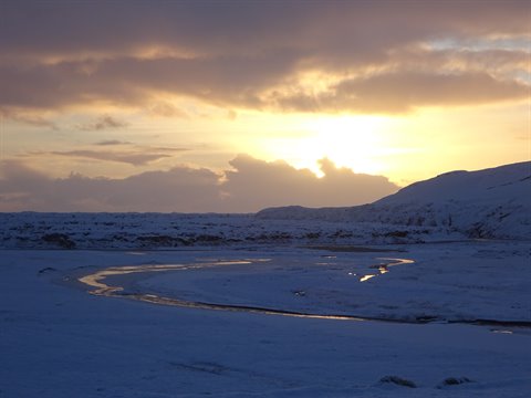 River winding through snow at golden dawn between snowy hills, low light