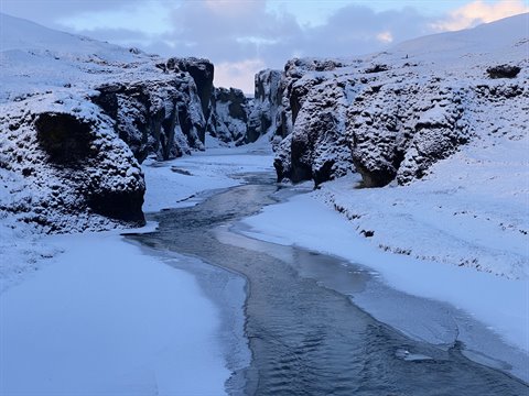 River flowing between snowy cliffs under cloudy sky, cold morning light, travel diary photo