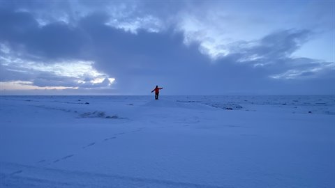 Traveler in red jacket walks across snowy plain under cloudy sky