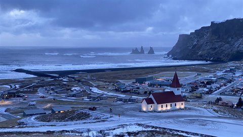 Red-roofed church lit among snowy houses and sea cliffs under cloudy skies