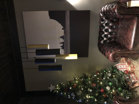 Decorated Christmas tree beside a leather Chesterfield armchair, painting and lamps, warm light