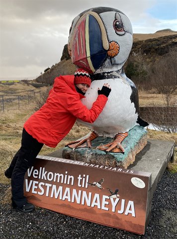 Woman in red jacket hugging a large puffin statue on a concrete base