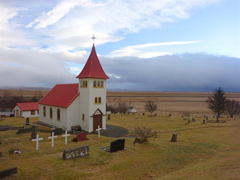 White church with red roof in churchyard under heavy clouds