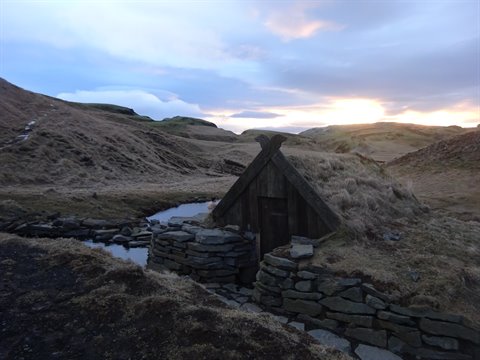 Traditional turf and stone hut among bare hills, golden light at horizon